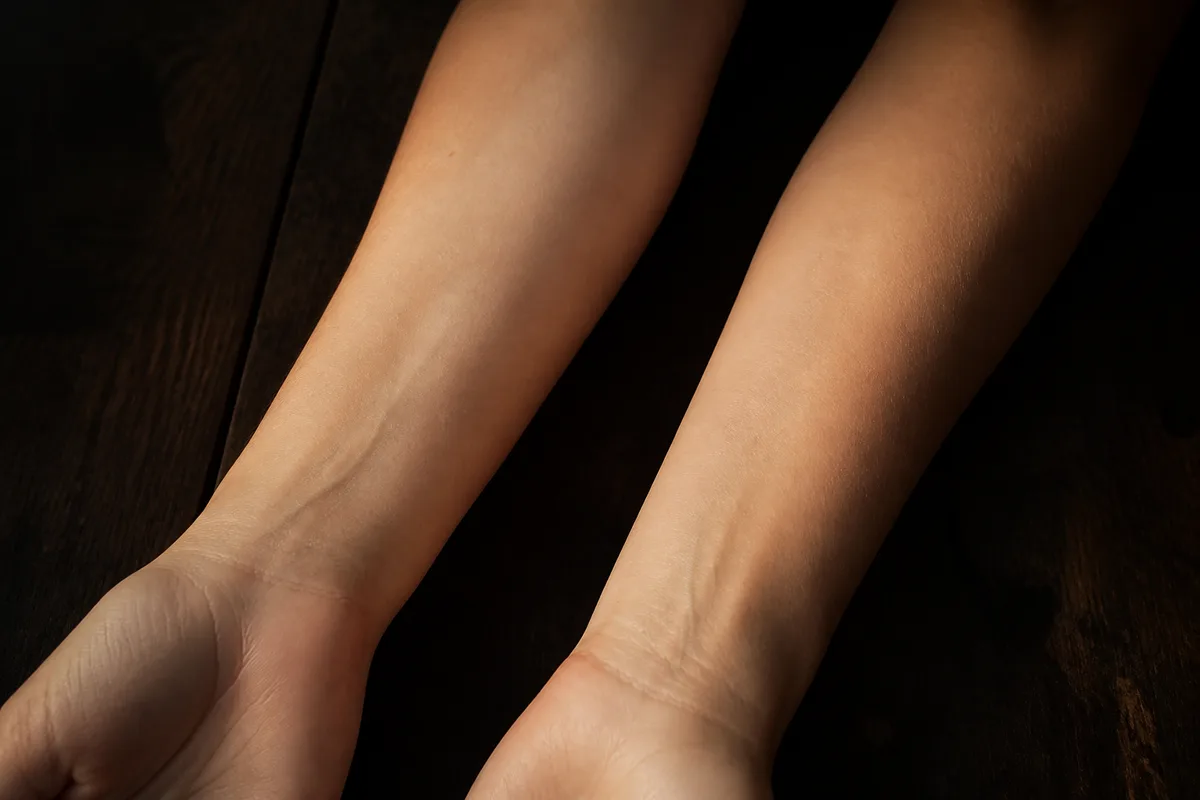 Poignet féminin et poignet masculin côte à côte, lumière douce de fin de journée, peau nue sans bijou